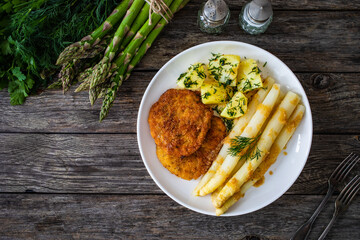 Fried schnitzel and white boiled asparagus with potato served on wooden table
