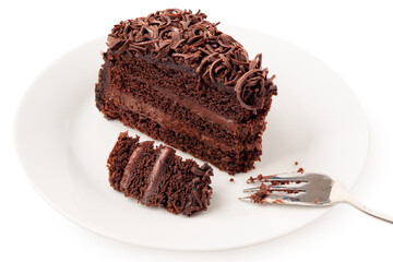 Slice of chocolate cake with cream filling and chocolate shavings next to fork on white plate. Partially eaten.