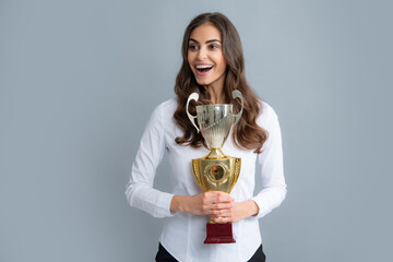 Portrait of happy young business woman with gold trophy cup on gray background.