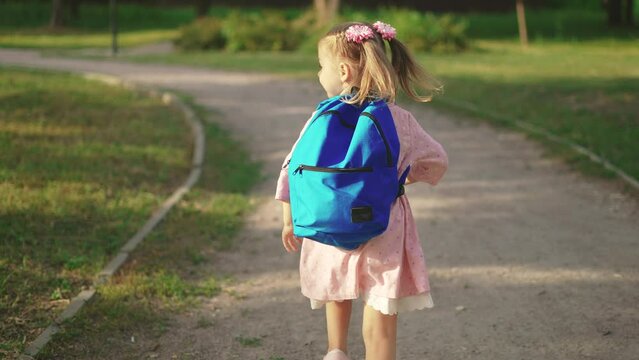 back to school. a little girl with a backpack runs through the green park to school along the path. education kid dream concept sun. a small child with a backpack back view runs the park to school