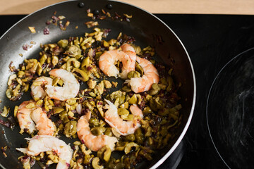 High angle close-up of shrimps with chopped olives and red onion in frying pan on electric cooker