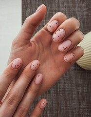Women`s hands with camouflage gel polish and black fragments on nails. Women's manicure with pale pink lacquer and black abstract design. Quail egg design