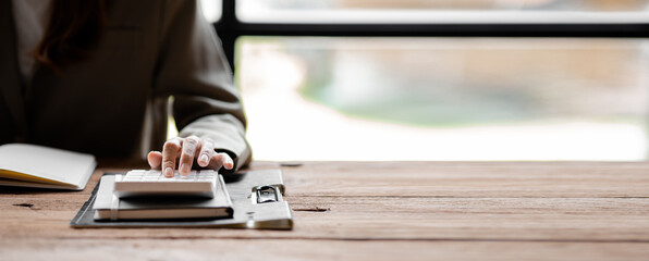 Businessman using a calculator to calculate numbers on a company's financial documents, he is...
