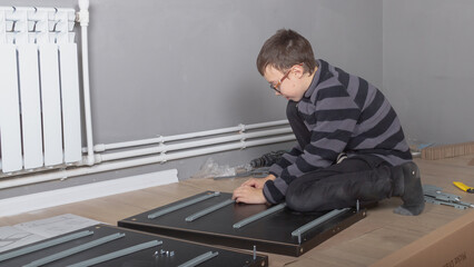 A teenage boy collects furniture for his room with a screwdriver connects the parts