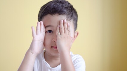 Cute boy smiling and covering his face on colour background. 