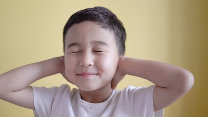 Cute boy covers ears with palms on colour background