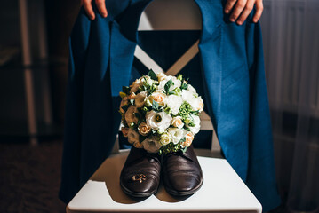 men's hands and shoes a bouquet and rings on a white pedestal. concept for event agency