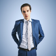 Young successfull businessman in blue suit and grey tie on blue background, close up