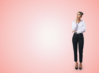 Thinking concept with pensive businesswoman in white shirt and dark trousers standing full length on abstract light pink wall backdrop, with empty place for you text, mock up - obrazy, fototapety, plakaty