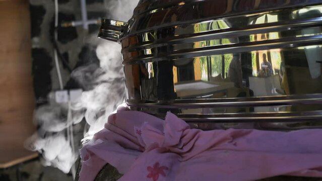 hot thick steam comes out of the cracks of the stone tonir closed with a stainless round hood and sealed with a cloth in the process of baking food in a stone tandoor. Steam in the sunshine