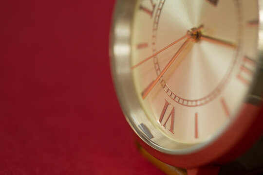 Extreme closeup of gold metallic second arrow passing by on clock face. Red background for copy space. macro watch.