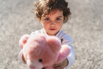 little female child gives her pink teddy bear looking to the camera - lifestyle concept of love and...