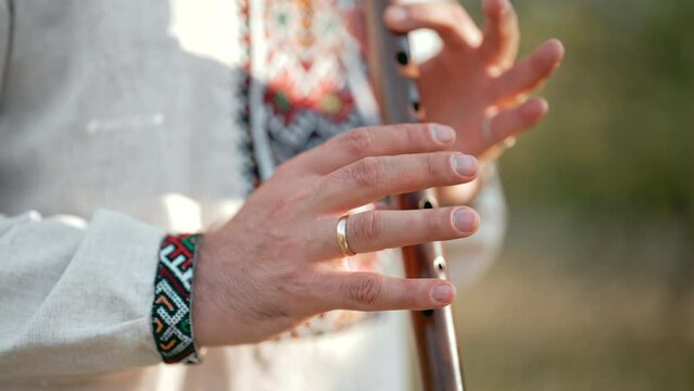 Hands of young man playing on woodwind wooden flute - ukrainian sopilka outdoors. Folk music concept. Musical instrument. Musician in traditional embroidered shirt - Vyshyvanka.