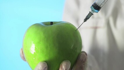 Close-up of a human in a medical coat and gloves injecting a syringe into an apple with some liquid on a blue background - Powered by Adobe