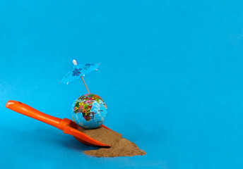 A globe on the sand under an umbrella from the sun on a blue background. Journeys. Summer holidays