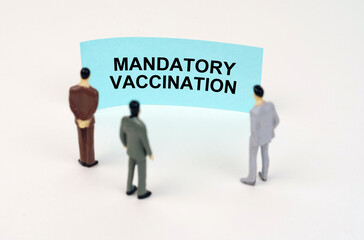 Miniature figures of people stand in front of a blue sign with the inscription - Mandatory Vaccination