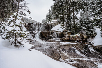 Winter waterfall called Certova strouha in Krkonose mountains,Czech Republic.Snowy frozen landscape.Frozen waterfall and wild stream,long exposure water.Czech National Park.Winter forest creek