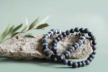 Two bracelets made of natural black volcanic lava stones beads isolated on pastel greenbackground. Handmade jewelry. Woman exoteric accessories. Talismans and amulets. Selective focus