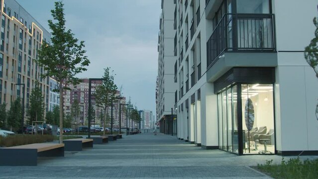 Apartment housing complex and sidewalk for pedestrians decorated by trees and benches near buildings. Stock footage. New city sleeping area.
