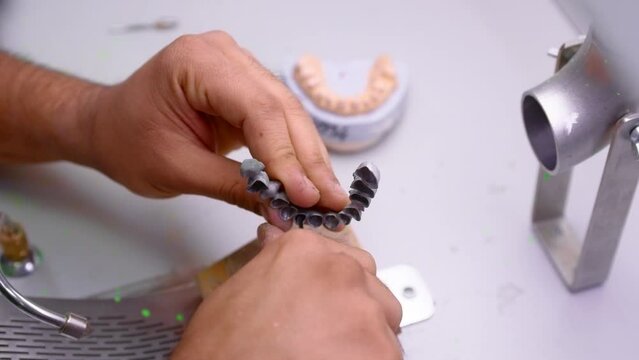 dental technician works in his workshop and makes artificial teeth for dentistry. in the frame are the hands of the master and the teeth created by the specialist. metal dentures. Slow motion