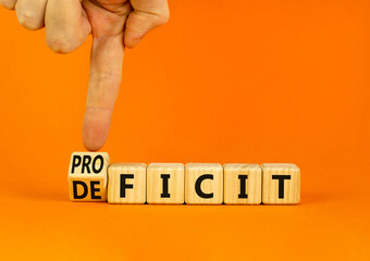 Proficit or deficit symbol. Businessman turns wooden cubes and changes the concept word deficit to proficit. Beautiful orange table orange background. Business proficit or deficit concept. Copy space.