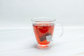 Tea bag in a double-walled glass mug with red tea on a white background