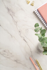 Business concept. Top view vertical photo of workspace pink planners pens gold binder clips and vase with eucalyptus on white marble background with copyspace