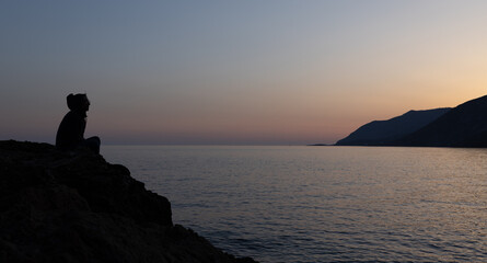 a man sits on a high seashore and watches the sunset, Greece, Crete, Chania