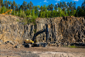 Basalt mining. Yellow excavators in a basalt quarry. Basaltic and sandstone rocks.