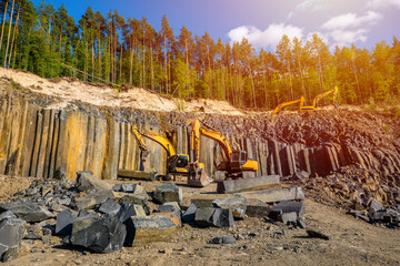 Basalt mining. Yellow excavators in a basalt quarry. Basaltic and sandstone rocks.