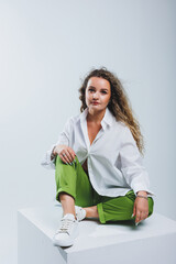 Positive woman with curly hair in a white light cotton shirt and trousers on a white isolated background. Women's casual wear.