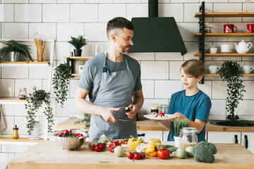 family dad young man and son teenage boy cook vegetable salad in kitchen and spend quality time together, father and son talking and cooking vegetarian food and doing chores, 8 march and mothers day