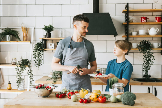 family dad young man and son teenage boy cook vegetable salad in kitchen and spend quality time together, father and son talking and cooking vegetarian food and doing chores, 8 march and mothers day - Powered by Adobe