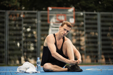 Fototapeta premium Sporty muscular man tying laces on sport sneakers before morning run at outdoor basketball court. Young fitness man training on fresh air.