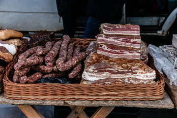 Big chunks of fresh salted bacon and cured sausage on a village market stall. Close-up. The fibrous texture of the bacon and spices is clearly visible. Natural food.