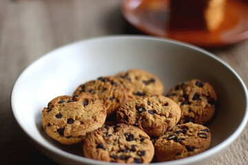 Bowl of chocolate chip cookies, plate of biscuits, open books and reading glasses on the table. Selective focus.