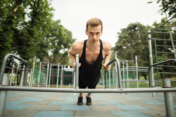 Handsome caucasian sports man doing push up exercise on parallel bars at outdoor gym, home workout...