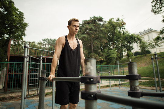 Fit man doing triceps dips on parallel bars at park exercising outdoors. Beautiful man doing work out and different exercises outdoor.