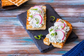 Appetizer, salted cottage cheese with dill, green onion and radish on wheat toast on a black stone board. Recipes with cottage cheese.