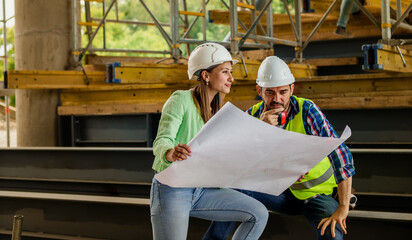 Woman architect explaining blueprint to supervisor at construction site. Engineer talking to contractor.