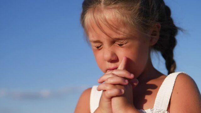 girl kid pray against a blue sky. child close-up concept faith religion and happy family. kid daughter jew crossed arms praying to god. kid pray worship and gratitude and catholic a happy childhood