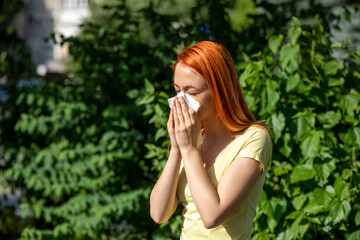 Young redhair woman sneezing in park. Pollen Allergy symptoms