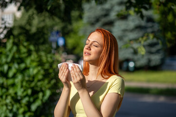 Young redhair woman sneezing in park. Pollen Allergy symptoms