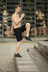 Attractive sporty muscular athlete stretches before a sports training session at a sports stadium, outdoor gym.