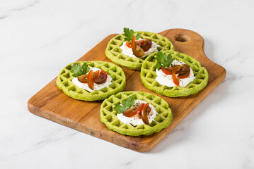 Round spinach waffles with cottage cheese, cherry tomatoes and parsley, on a wooden board. Light background