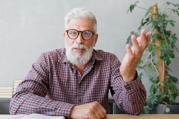 man with gray hair is working in an office on a laptop and talking on the phone. an adult male director or businessman is negotiating on an online webcam. business and finance of a male lawyer or