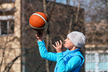 A young girl in a blue outerwear 10-11 years old holds a basketball in her hands. Child playing...