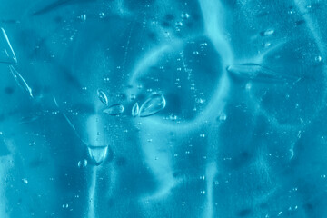 Texture of transparent antiseptic gel with air bubbles on blue background. Summer ocean imitation. Concept of skin moisturizing, prevention of virus. Liquid beauty product closeup. Backdrop, flat lay