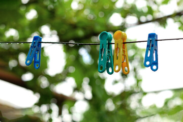 Multi-colored plastic clothespins hang on a rope after rain on a green blurred background