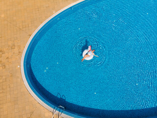 Summer holidays, relaxation. Woman on unicorn pool float in pool. Enjoying summer vacations during quarantine. Aerial top view from drone